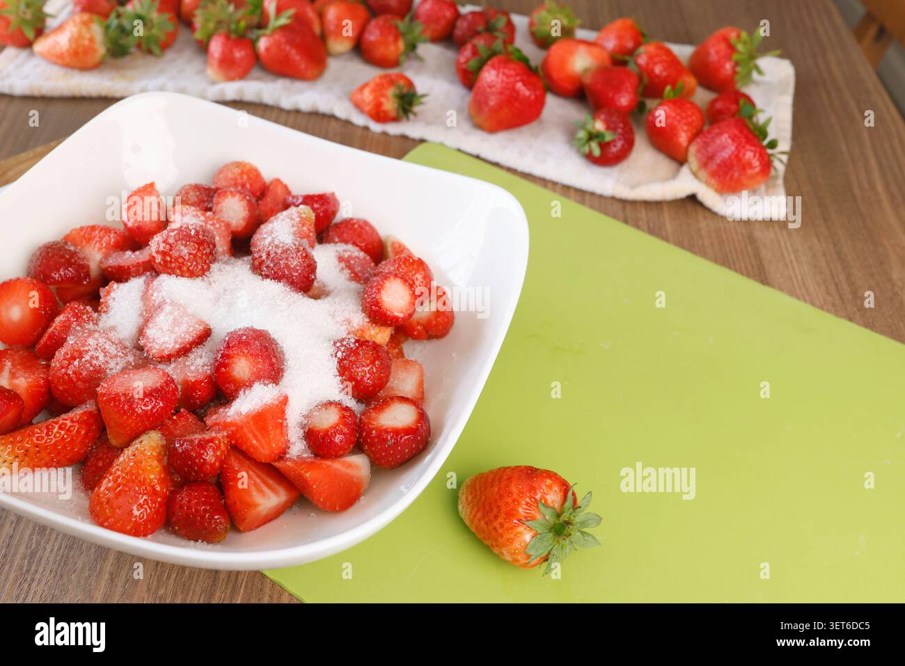 Frisch geschnittene Erdbeeren mit weißem Zucker in einer Keramikschale auf dem Küchentisch. Traditionelle Routine zur Konservierung von Beeren im Sommer, die elegant ist Stockfoto