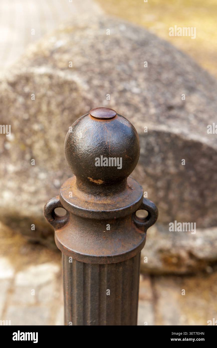 Eine Makroaufnahme einer verwitterten metallischen Säulenbarriere mit Textur und einem großen Felsbrocken im weichen Fokus dahinter. Stockfoto