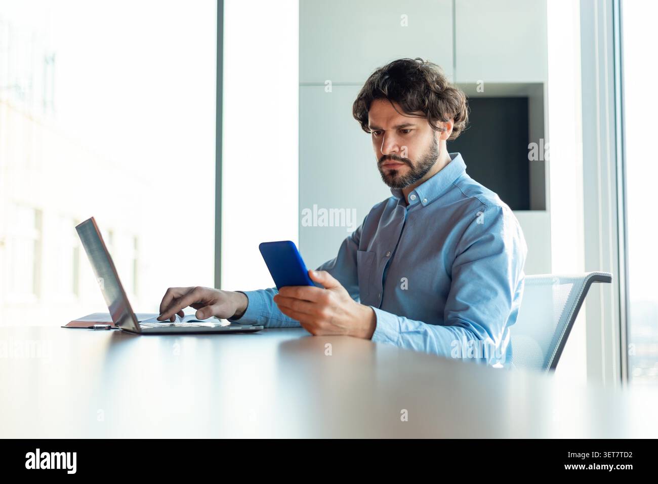 Fokussierter Hispanischer Mann, Der Smartphone Verwendet, Während Er Am Schreibtisch Arbeitet, Business Concept Stockfoto