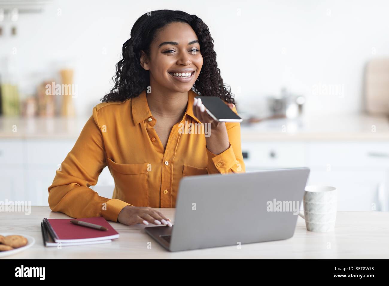 Lächelnde Junge Schwarze Frau Mit Smartphone Und Laptop Im Home Office, Arbeitskonzept Stockfoto
