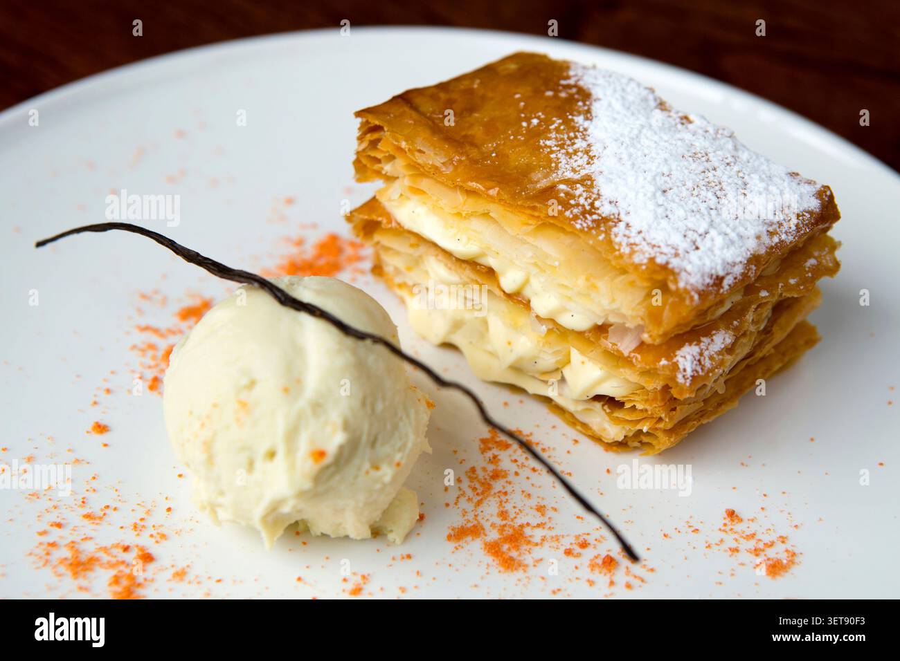 Ein Mille-Feuille-Dessert steht auf einem Teller neben einer Schaufel Vanilleeis. Die Blätterteigschichten sind mit Creme gefüllt. Stockfoto