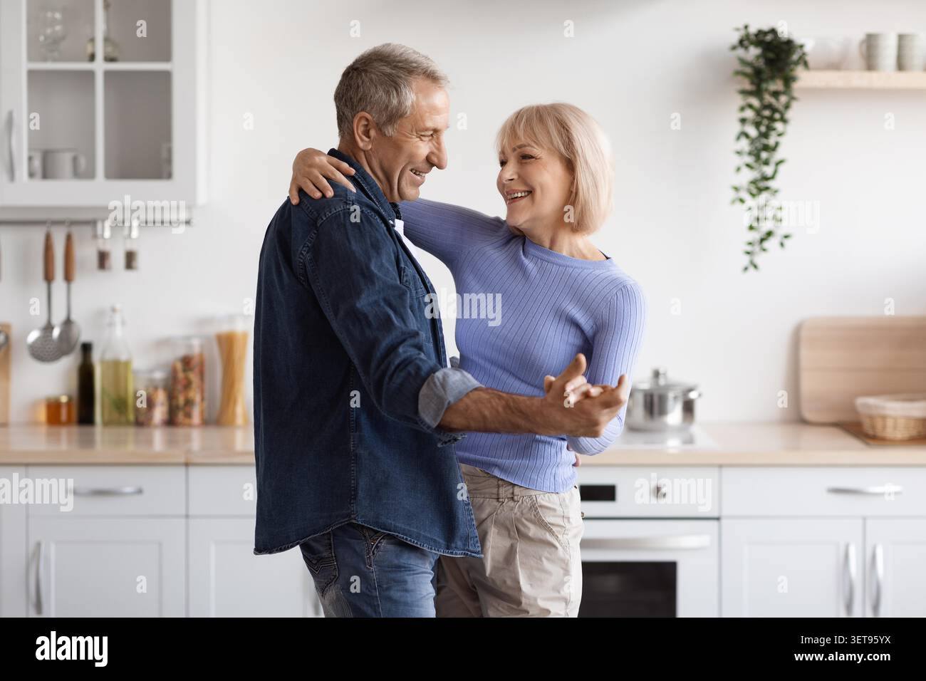 Glückliches Älteres Kaukasisches Paar, Das Zusammen In Der Küche Tanzt, Fröhlicher Lebensstil Zu Hause Stockfoto
