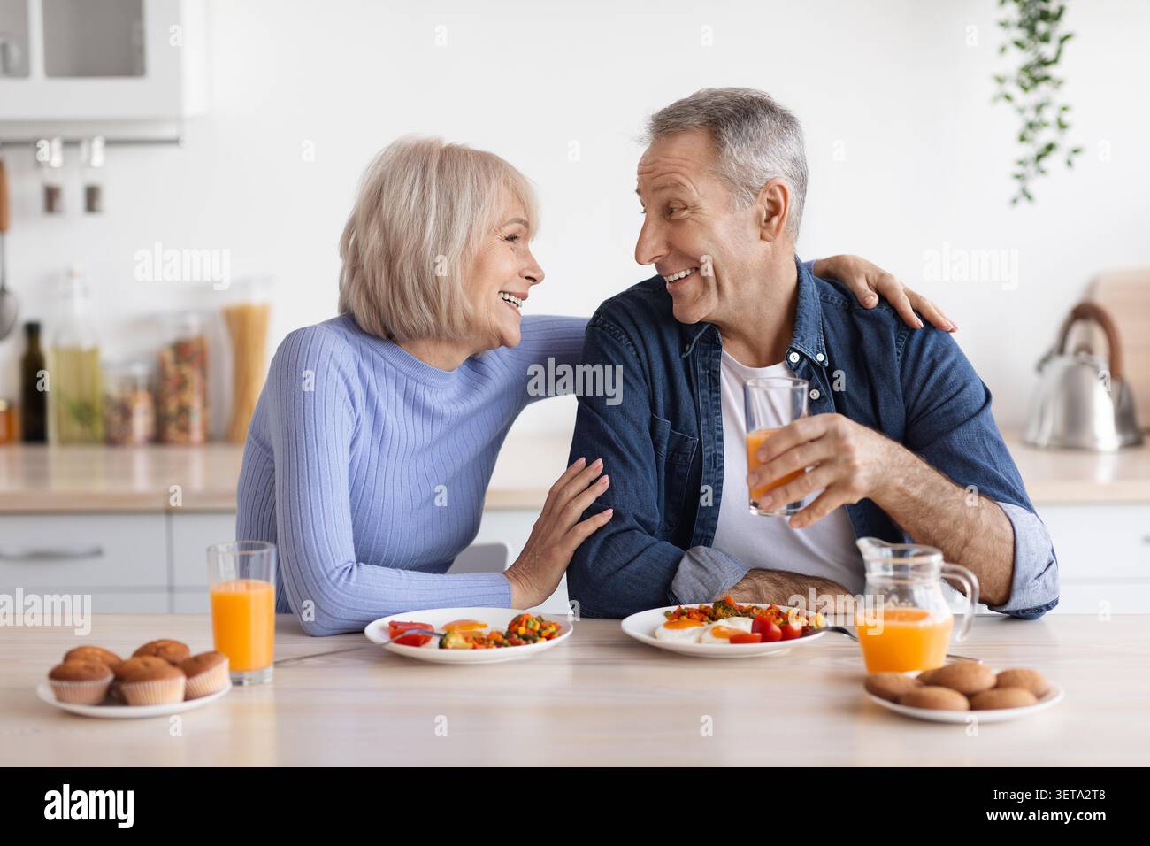 Glückliches Älteres Kaukasisches Paar Genießt Gemeinsam Frühstück In Der Küche, Lächeln Und Momente Teilen Stockfoto