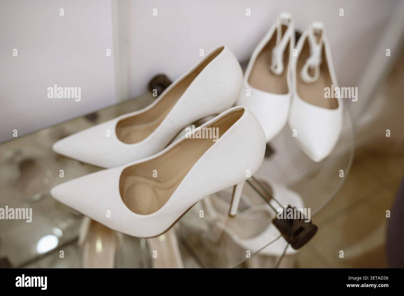 Weiße Schuhe mit hohem Absatz. Elegante und stilvolle Hochzeitsschuhe. Zwei Paar weiße Hochzeitsschuhe auf einer Glasoberfläche. Hochzeitsvorbereitung. Hochzeitsschuh Sal Stockfoto