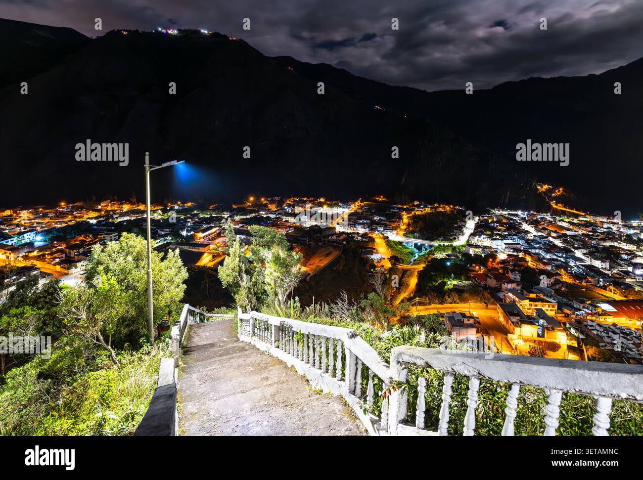 Ein beleuchteter nächtlicher Blick auf die Bergstadt Banos de Agua Santa in Ecuador, gesehen von einem hohen malerischen Ausblick mit Treppen im Vordergrund. Stockfoto