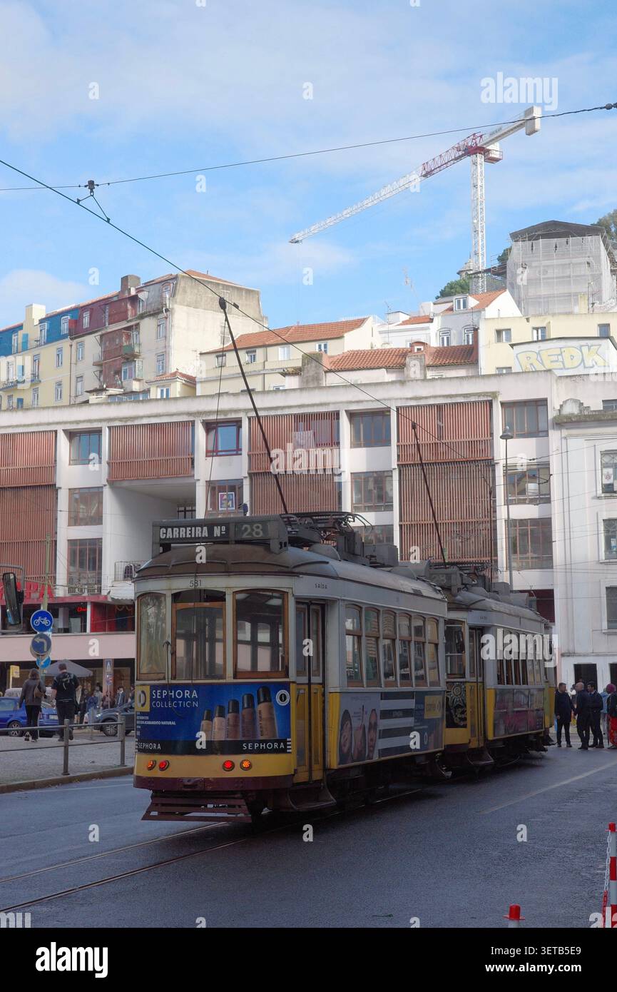 Berühmte gelbe Straßenbahn Nr. 28 von Lissabon mit Werbung auf der Straße mit elektrischen Kabeln und historischen Gebäuden Stockfoto