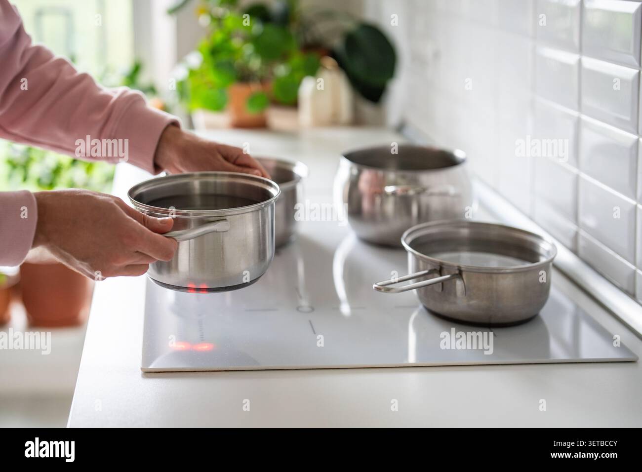 Mann, der den Topf mit kaltem Wasser zum Kochen auf den Herd stellt, geplanter Ausfall des Warmwassersystems im Haus. Stockfoto