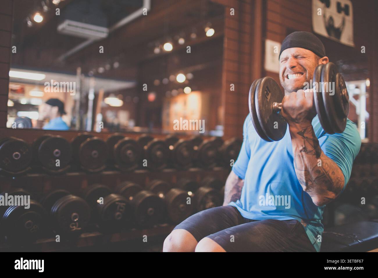 Muskulöser tätowierter Mann, der Bizepslocken im Fitnessstudio macht Stockfoto