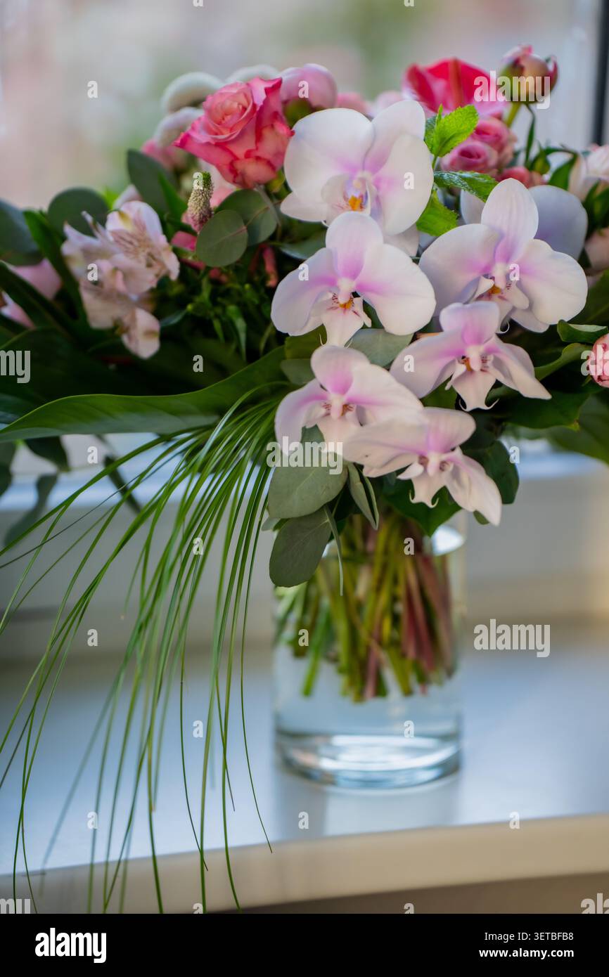 Wunderschönes Blumenarrangement mit zarten Orchideenblüten und kleinen Rosenknospen, das professionelle Blumenhandwerk und elegante Geschenkkonzepte präsentiert Stockfoto