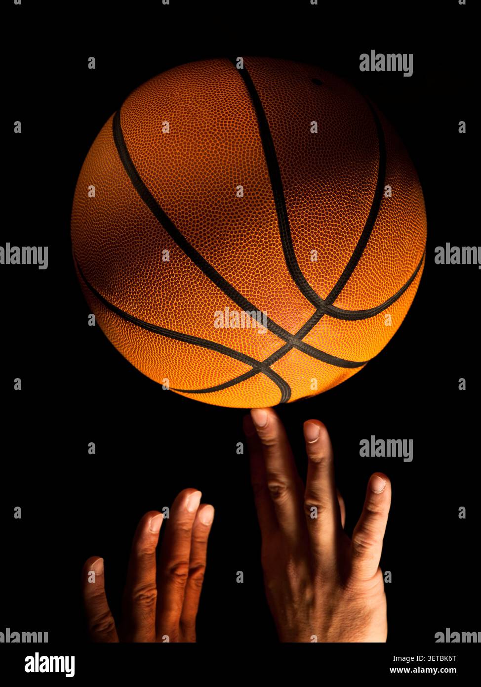 Hände greifen nach einem Basketball vor schwarzem Hintergrund Stockfoto