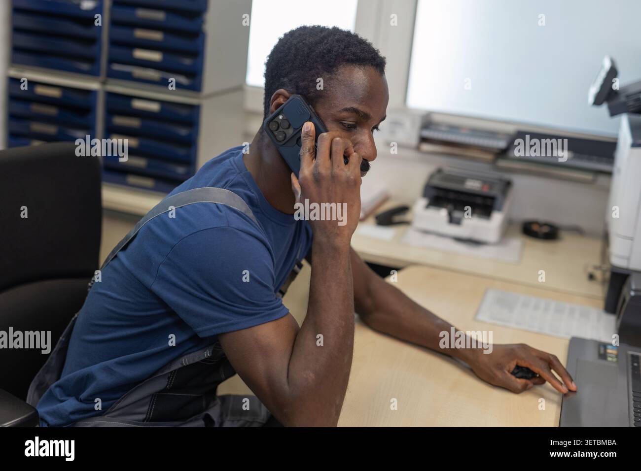 Ein männlicher Automechaniker telefoniert mit einem Kunden, während er an einem Computer in einer Autowerkstatt arbeitet. Stockfoto