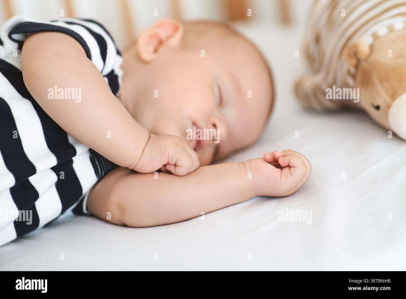 Das Baby schläft friedlich neben Plüschtier in ruhiger Umgebung im Kinderzimmer während der Tageslichtstunden Stockfoto