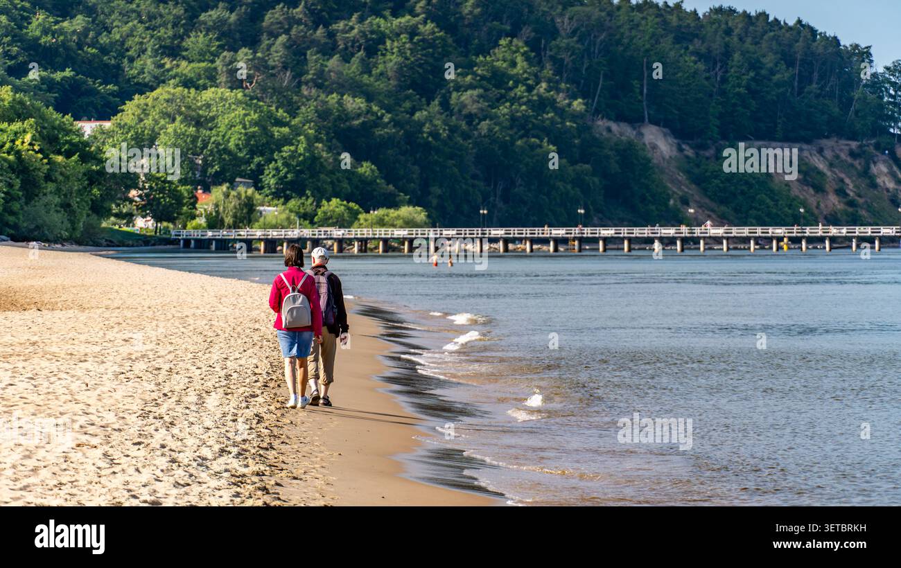 Seniorenpaar spazieren am Ostseestrand mit Rucksäcken am sonnigen Tag Stockfoto
