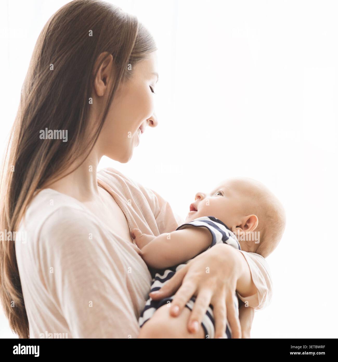 Mutter hält ihr Baby in einem ruhigen Moment liebevoll in einer hellen, natürlichen Umgebung Stockfoto