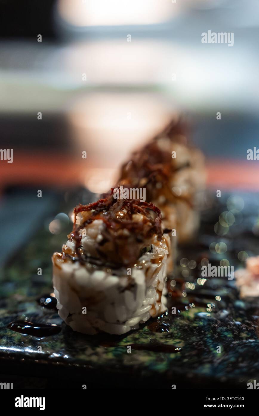 Sushi-Brötchen mit knusprigen gebratenen Zwiebeln auf dunklem Teller, maledivisches Essen Stockfoto
