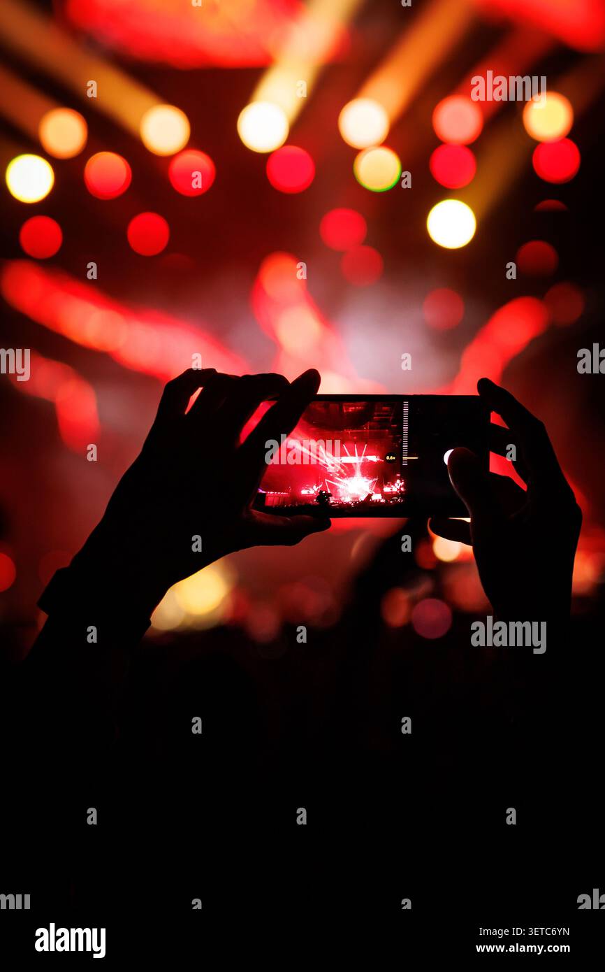 Smartphone nimmt Live-Konzert mit verschwommenen roten Lichtern auf Stockfoto