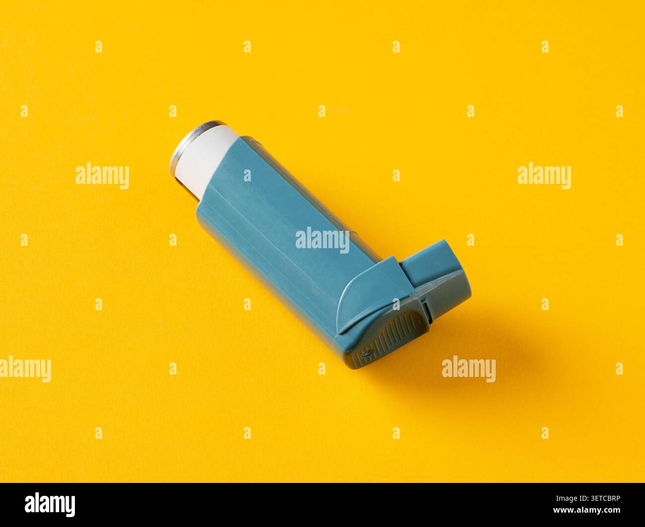 Nahaufnahme eines blauen Asthma-Inhalators auf einem leuchtend gelben Hintergrund, der die Bedeutung des Atemwegs-Gesundheitsmanagements unterstreicht Stockfoto