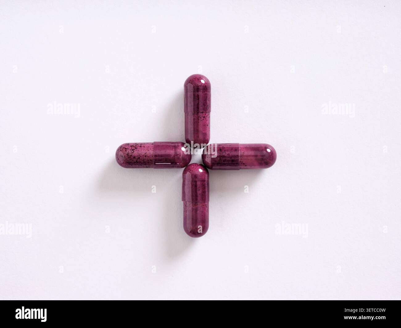 Vier rote Pillen, kreuzförmig auf weißem Hintergrund angeordnet, repräsentieren Gesundheitsfürsorge, Medizin und Arzneimittel Stockfoto