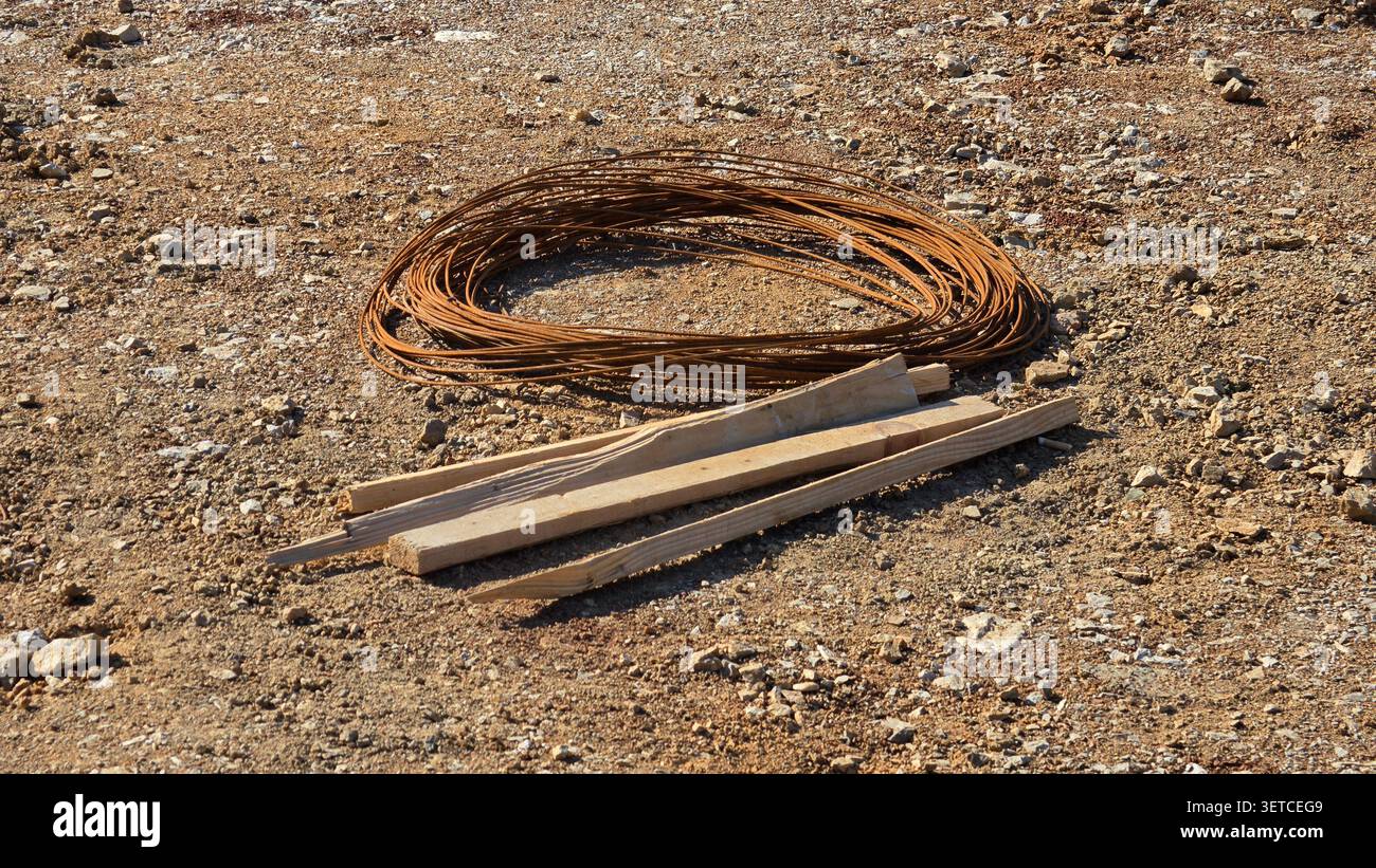 Auf der kiesigen Oberfläche einer Außenbaustelle befindet sich neben mehreren spitzen Holzpfählen ein Bündel aus rostigem Stahldraht Stockfoto
