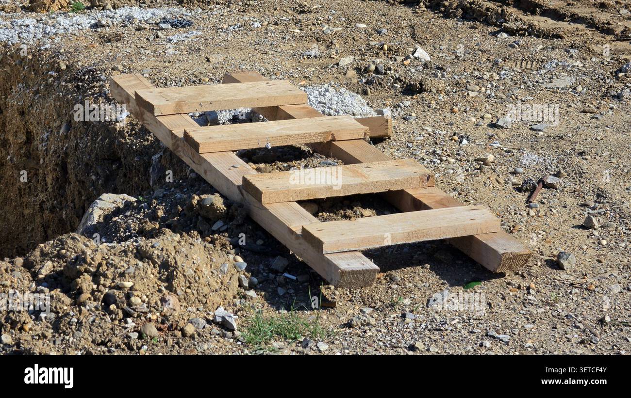 Eine provisorische kurze Holzleiter liegt flach über ausgehobenem Boden und felsigem Boden auf einer Außenbaustelle Stockfoto