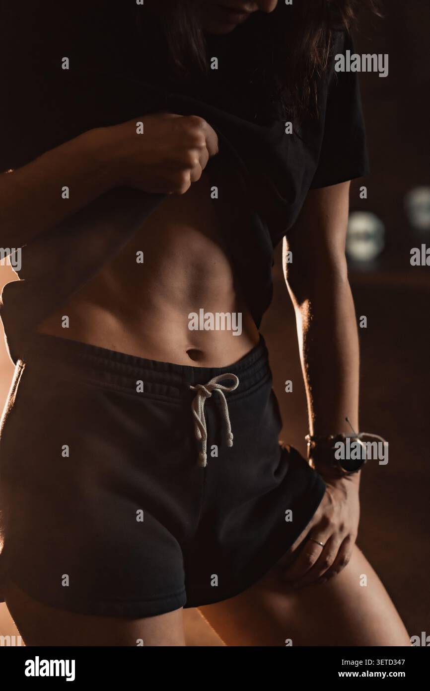 Nahaufnahme einer Frau in schwarzer Shorts und T-Shirt, die definierte Bauchmuskulatur im Fitnessstudio hervorhebt. Perfekt für Themen wie Kraft, Wellness und aktive Lebensmotivation Stockfoto