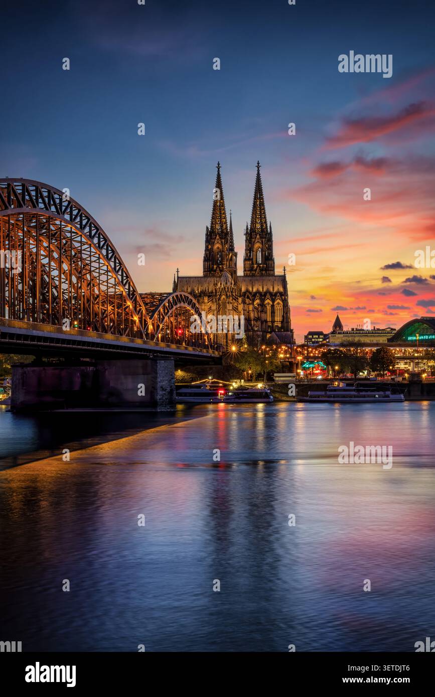 Der beleuchtete Kölner Dom mit der Hohenzollernbrücke und dem Rhein in der Sommerdämmerung Stockfoto