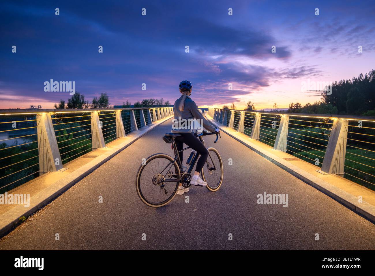 Radfahrerin mit Rennrad auf beleuchteter Brücke bei Sonnenuntergang Stockfoto