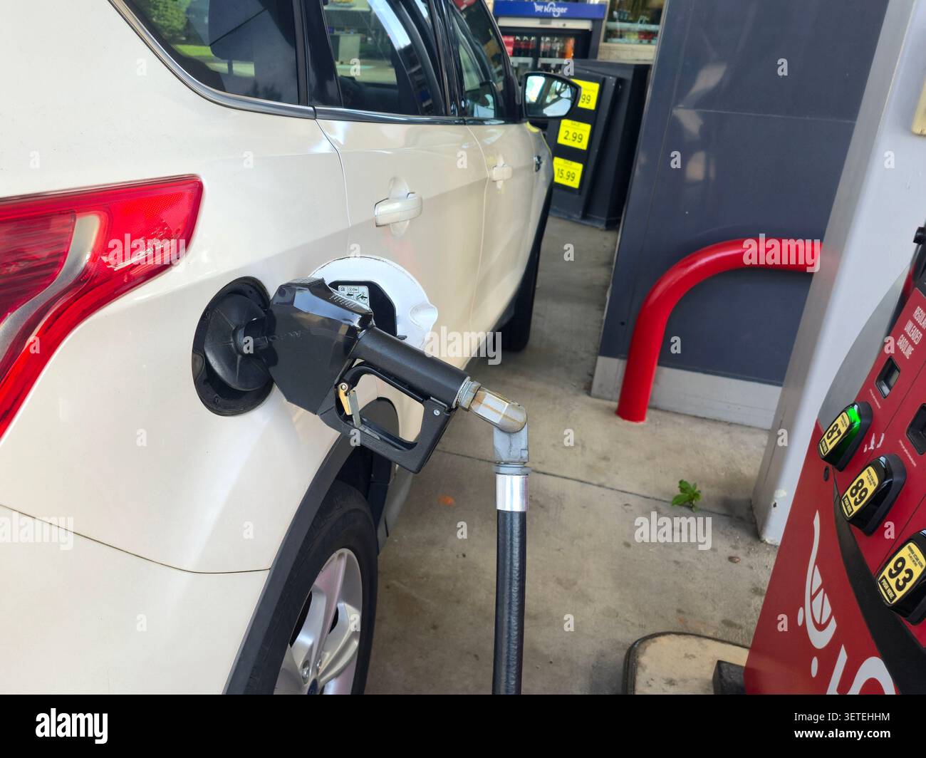 Ein weißer SUV, der an einer Tankstelle in den Vereinigten Staaten betankt wird. Die Marke für Kraftstoffpumpe und Lebensmittelgeschäft ist in einem Kroger-Tankzentrum sichtbar - Smartphone-aufgenommenes Stockfoto