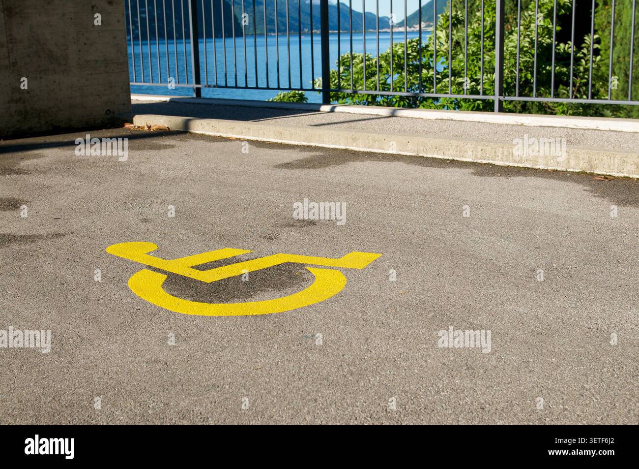 Blick auf ein gelbes Symbol für Behinderte am Boden am Luganer See, Schweiz. Ein konzeptionelles Bild, das Behindertenvorschriften und t gegenüberstellt Stockfoto