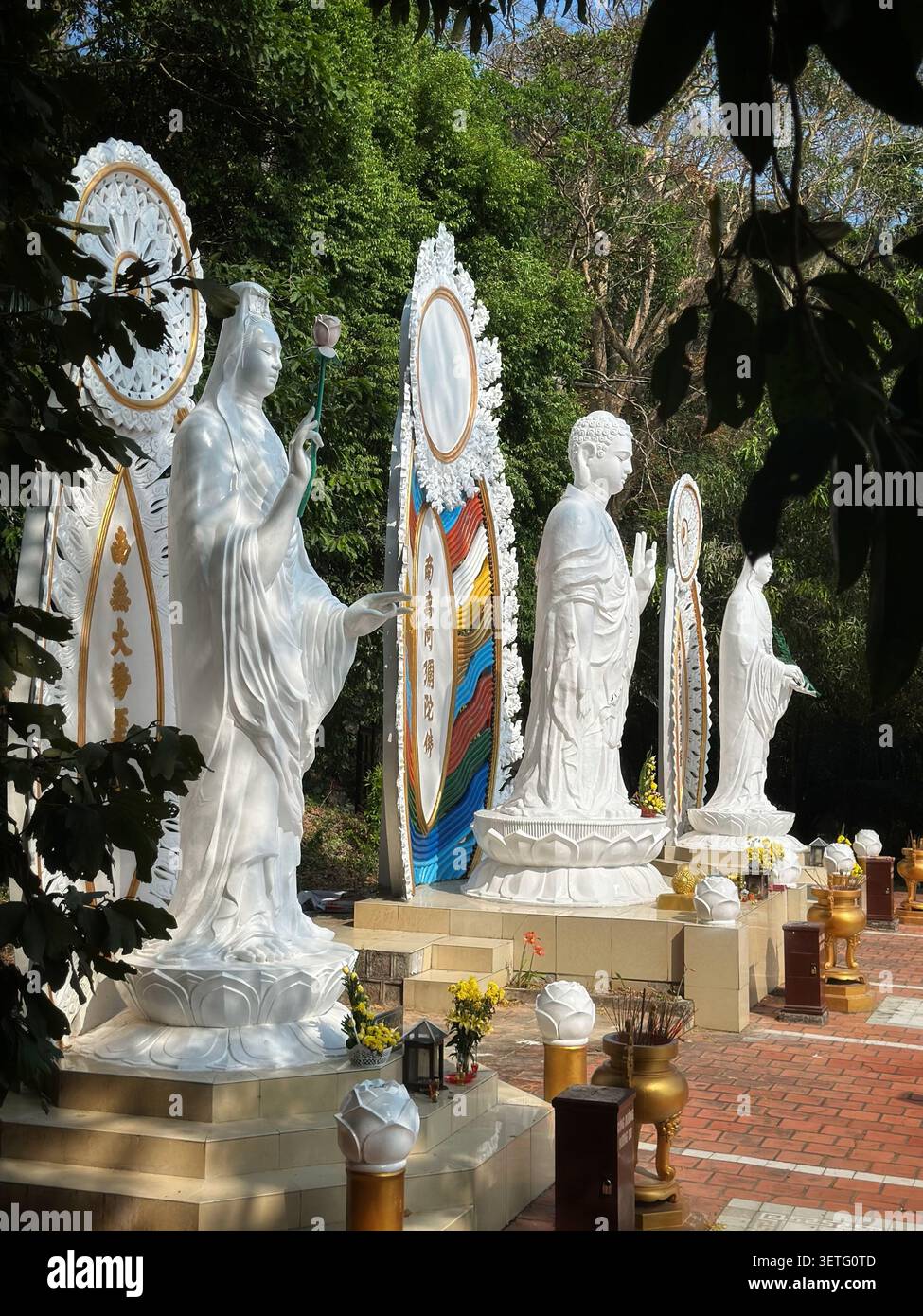 Weiße buddhistische Statuen stehen auf Lotussockeln in einem Tempelgarten. Drei elegante weiße Marmorstatuen buddhistischer Gottheiten stehen hintereinander. Sie fea - Smartphone-aufgenommenes Stockfoto