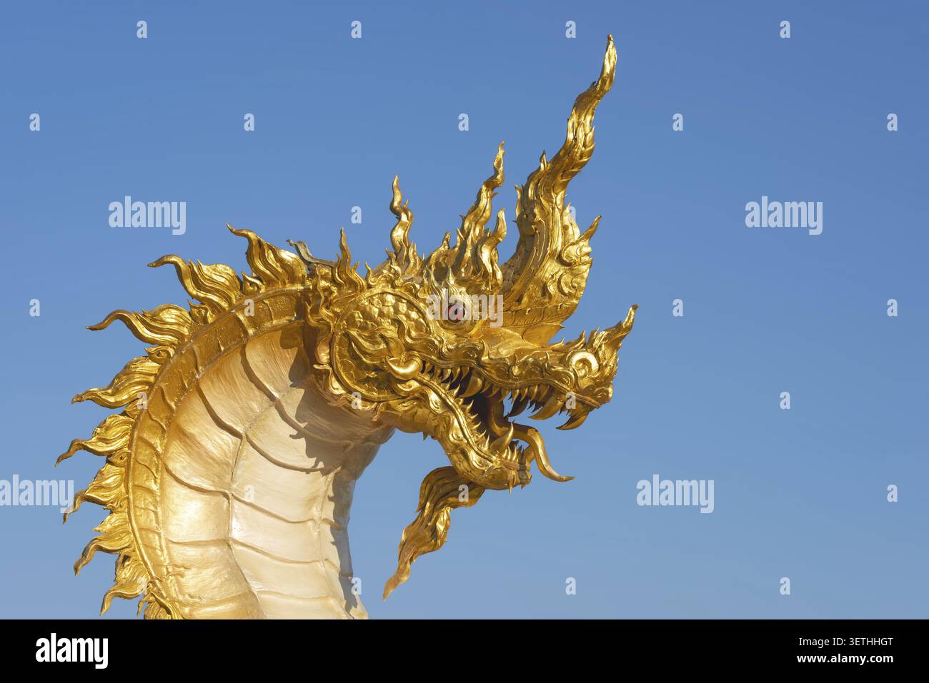 Der goldene Naga-Drache erhebt sich über den klaren Himmel der Khao Kho Berge. Die flammenartigen Ornamente, die roten Augen und die fein geformten Skalen spiegeln das wider Stockfoto