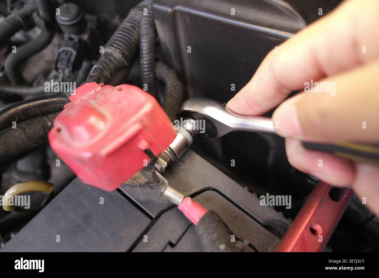 Lösen oder ziehen Sie bei der Autoreparatur mit einem Ratschenschlüssel eine Schraube an einem Autobatterieanschluss fest Stockfoto