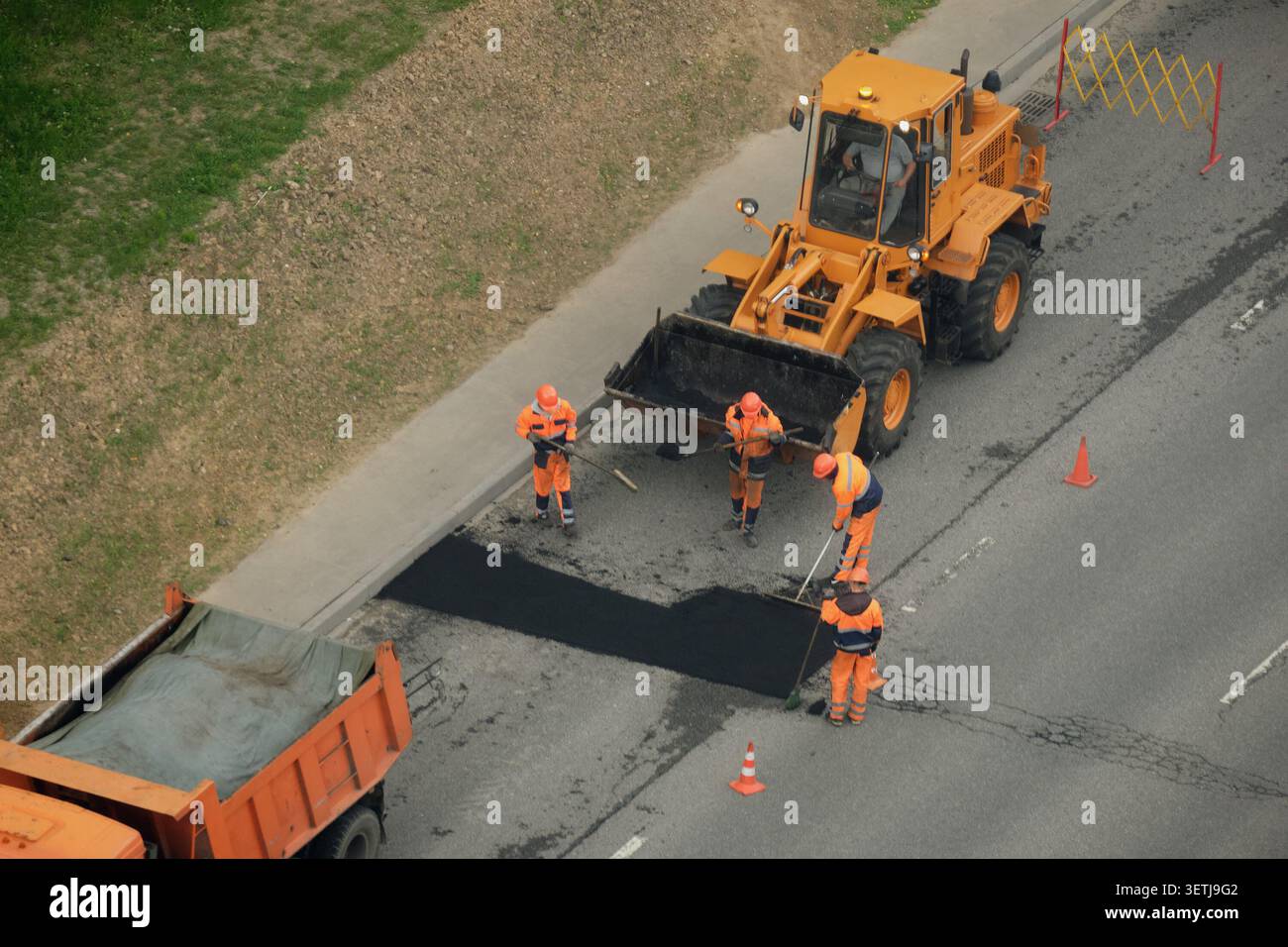 Straßenarbeiterteam pflastert Asphalt auf der Stadtstraße. Baupersonal repariert Oberflächen mit schweren Maschinen und Planierraupen. Entwicklung städtischer Infrastruktur Stockfoto