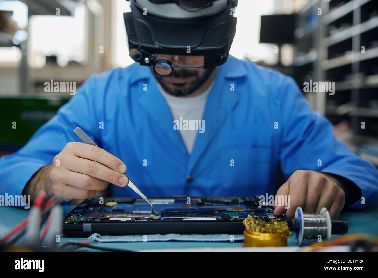 Techniker Mann Löttechniker in einem blauen Labormantel repariert einen Laptop sorgfältig Stockfoto