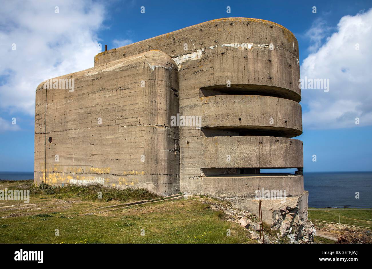 Deutsche Kanone aus dem Zweiten Weltkrieg zielen auf das Gebäude in Alderney mit Blick auf die felsige Küste unter einem rostenden Kriegskran Stockfoto