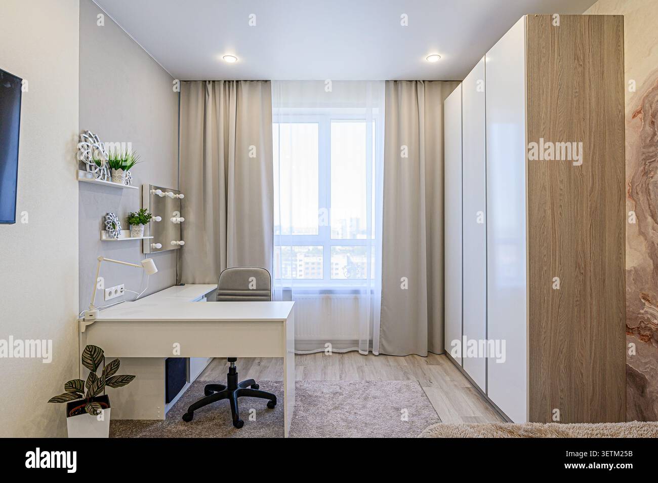 Helles Zimmer mit weißem Schreibtisch, Stuhl, Fenster und Stauraum. Neutrale Farbpalette Stockfoto