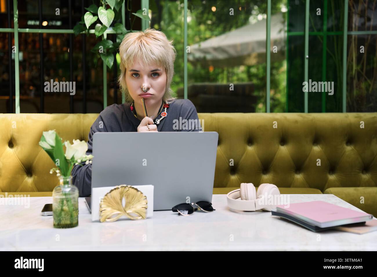 Eine junge, schöne, nicht binäre Person entspannt sich in einem stilvollen Café und genießt einen Moment der Kreativität. Stockfoto