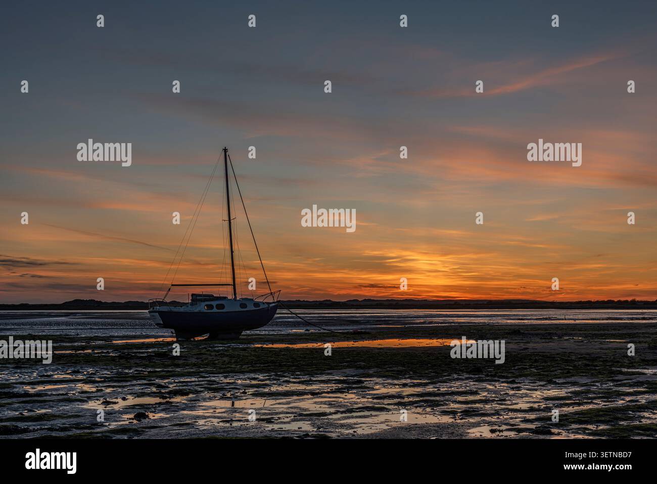 Sonnenuntergang hinter Dünen an der Westküste Englands; feuchtes Wattenmeer im Vordergrund reflektieren das untergehende Sonnenlicht; verankerte Yacht in partieller Silhouette Stockfoto