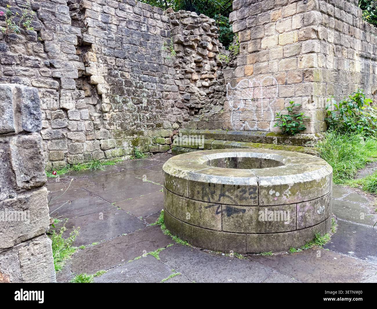 Historischer kreisförmiger Steinbrunnen, der sich gegen alte Mauerruinen befindet. Newcastle upon Tyne, Tyne and Wear, England. Stockfoto