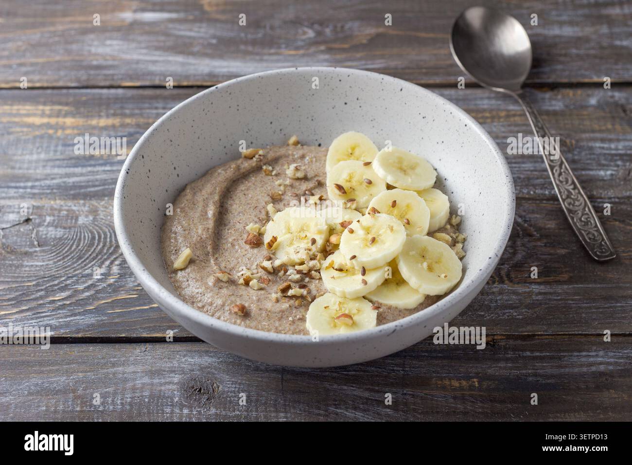 Gesunder Leinbrei mit Bananenscheiben, gehackten Nüssen und Samen in einer Keramikschale. Nahrhaftes Frühstück mit natürlichen Zutaten, Kopie Stockfoto