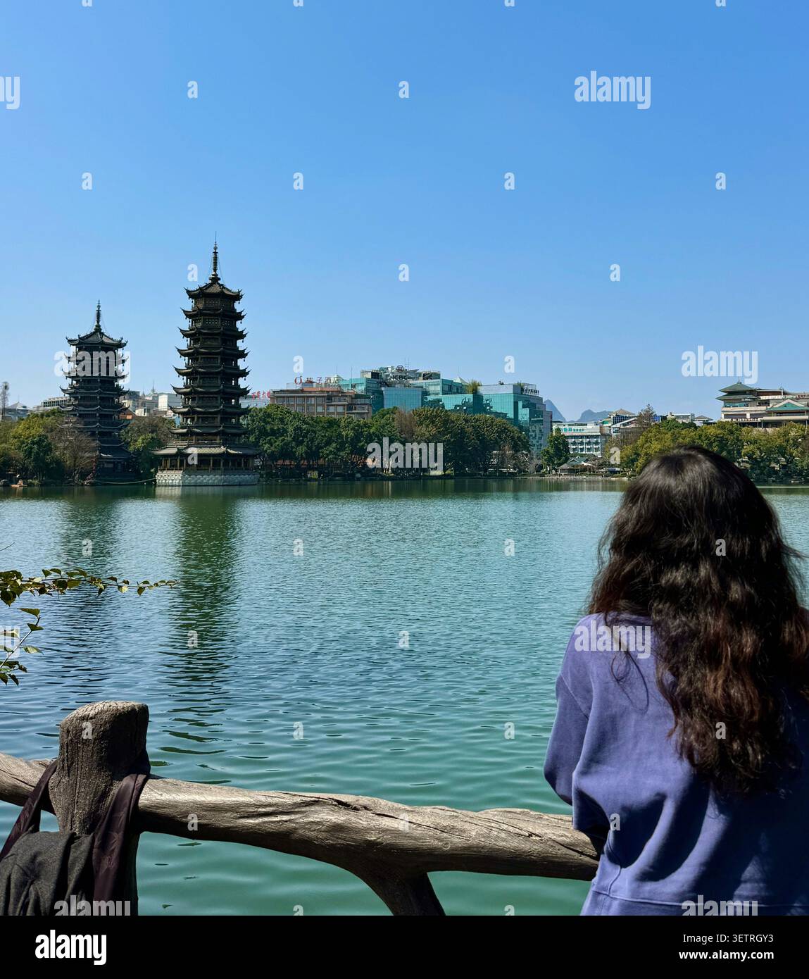 Touristen-Frau von hinten gesehen, die Sonne- und Mondpagoden über dem Rong-See, Guilin-Wahrzeichen, Guangxi, China ansieht - Smartphone-aufgenommenes Stockfoto