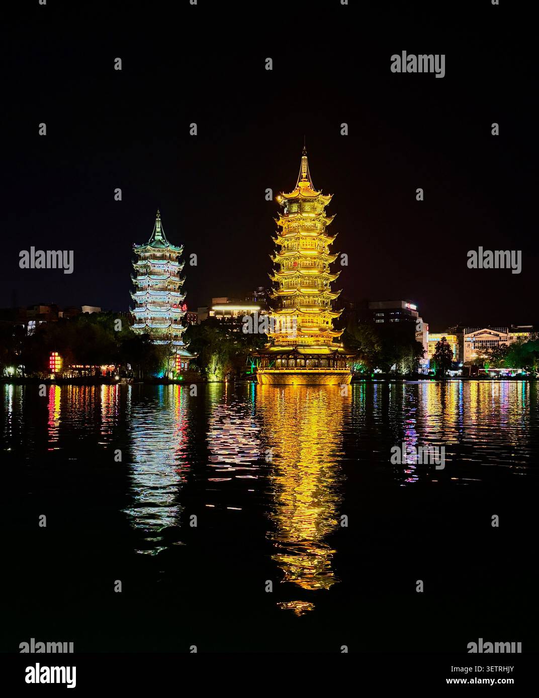 Sonnen- und Mond-Pagoden bei Nacht beleuchtet mit goldenen Spiegelungen auf dem Rong See, einem ikonischen Wahrzeichen von Guilin, Guangxi, China - Smartphone-aufgenommenes Stockfoto