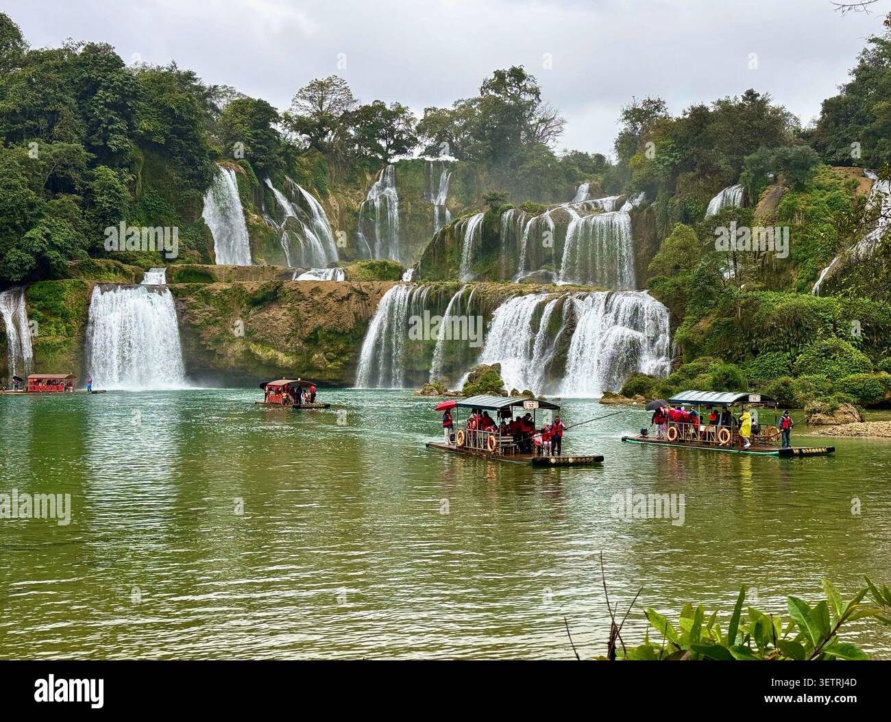 Sightseeing-Rafts mit Touristen vor der majestätischen mehrstufigen Detian-Wasserfall-Kaskade - Smartphone-aufgenommenes Stockfoto
