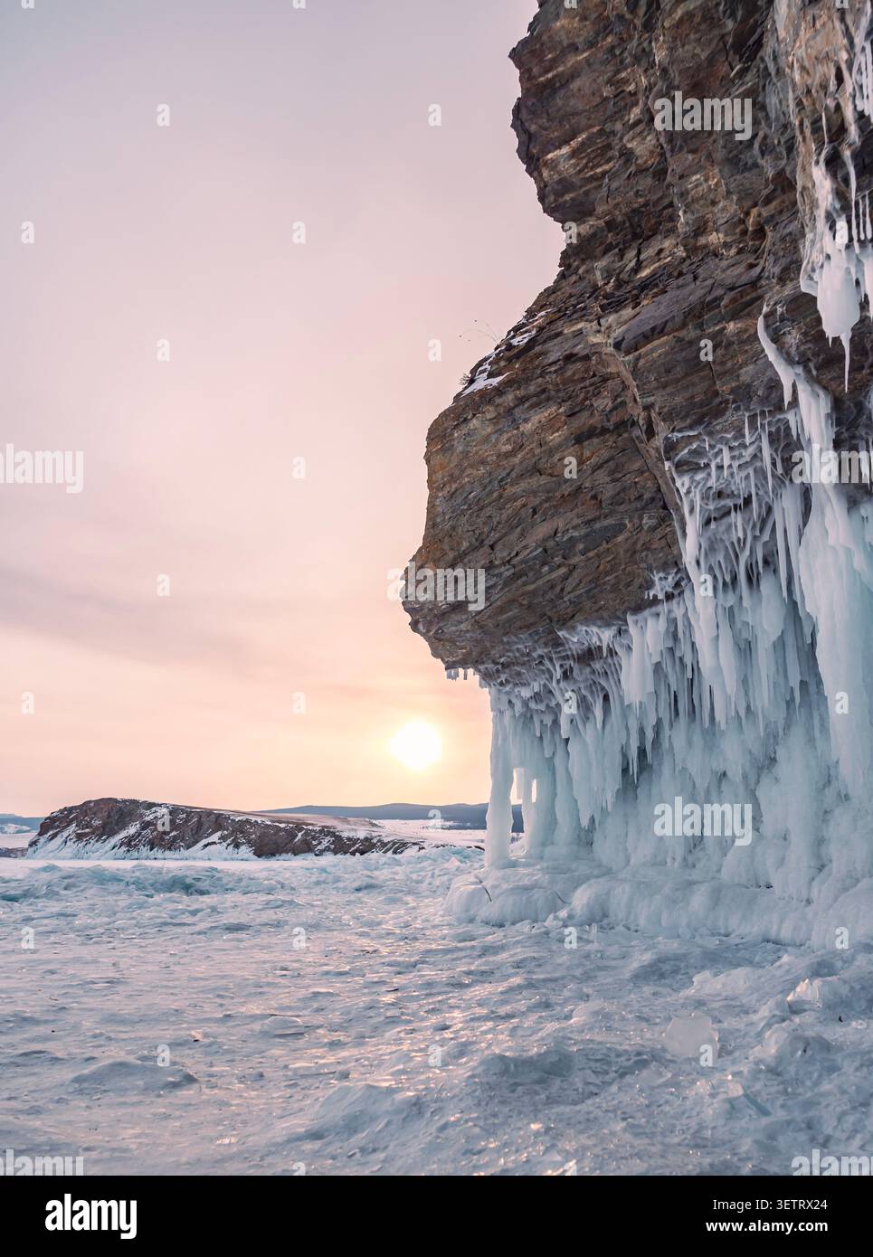 Dramatische Eisformationen stehen im Kontrast zu zerklüfteten Klippen in einer Winterlandschaft bei Sonnenaufgang Stockfoto