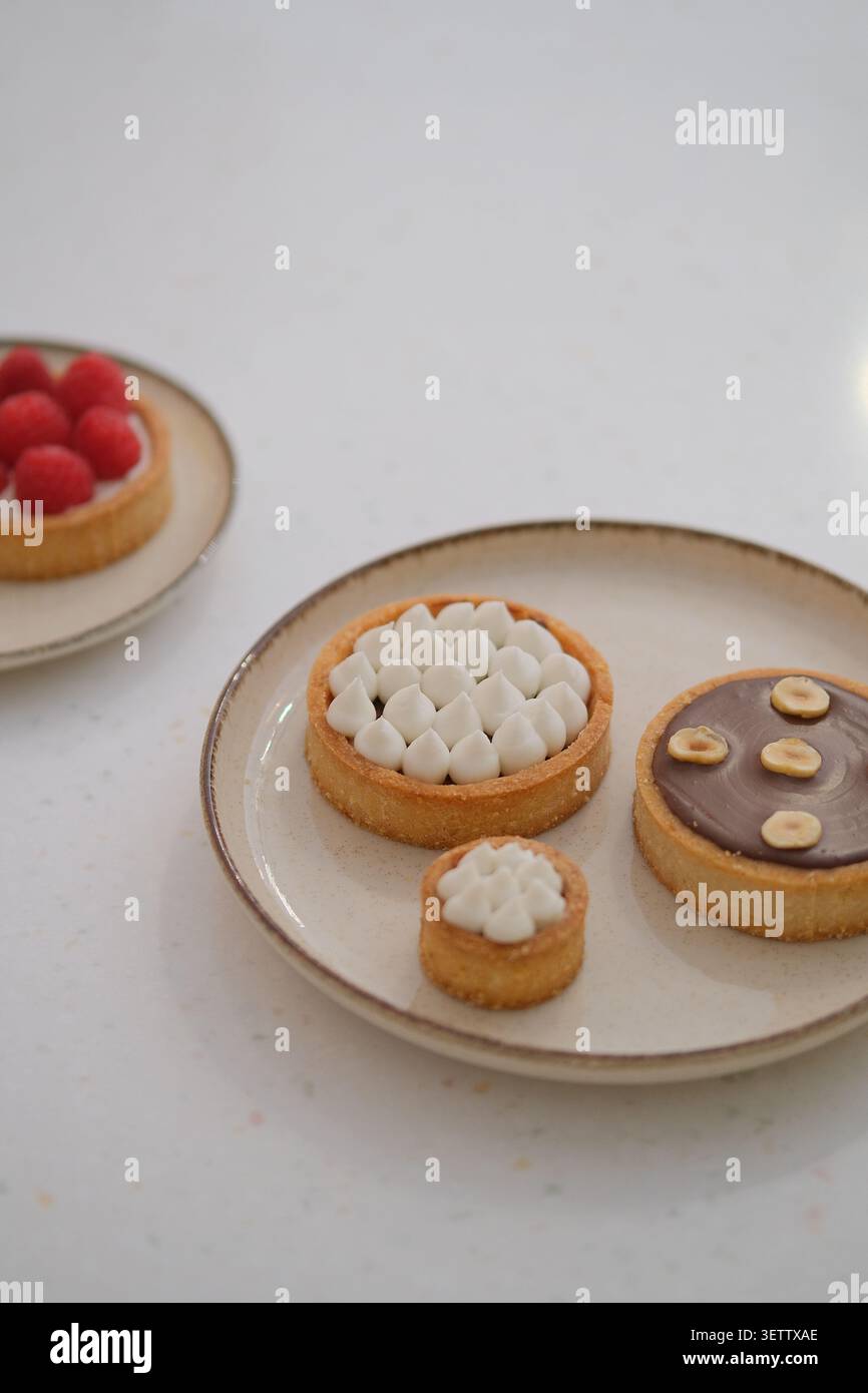 Elegante Auswahl an kleinen Teigkuchen auf Keramikplatten mit Sahne, Schokolade und Himbeeren Stockfoto
