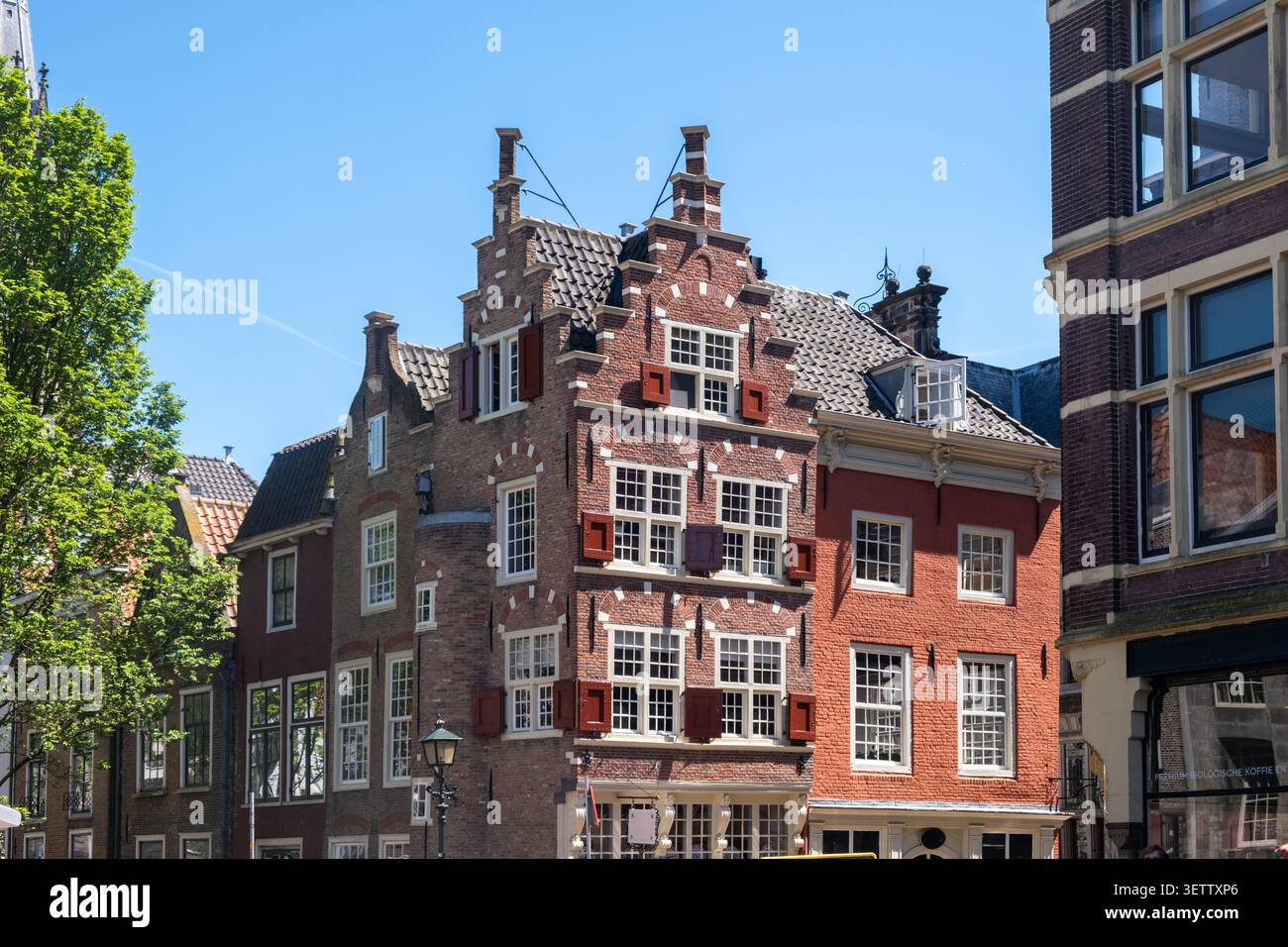 Delfter Rathausfassade mit Säulen, Skulpturen, vergoldeten Ornamenten und roten Fensterläden vor blauem Himmel im Stadtzentrum von Delft, Niederlande. Stockfoto