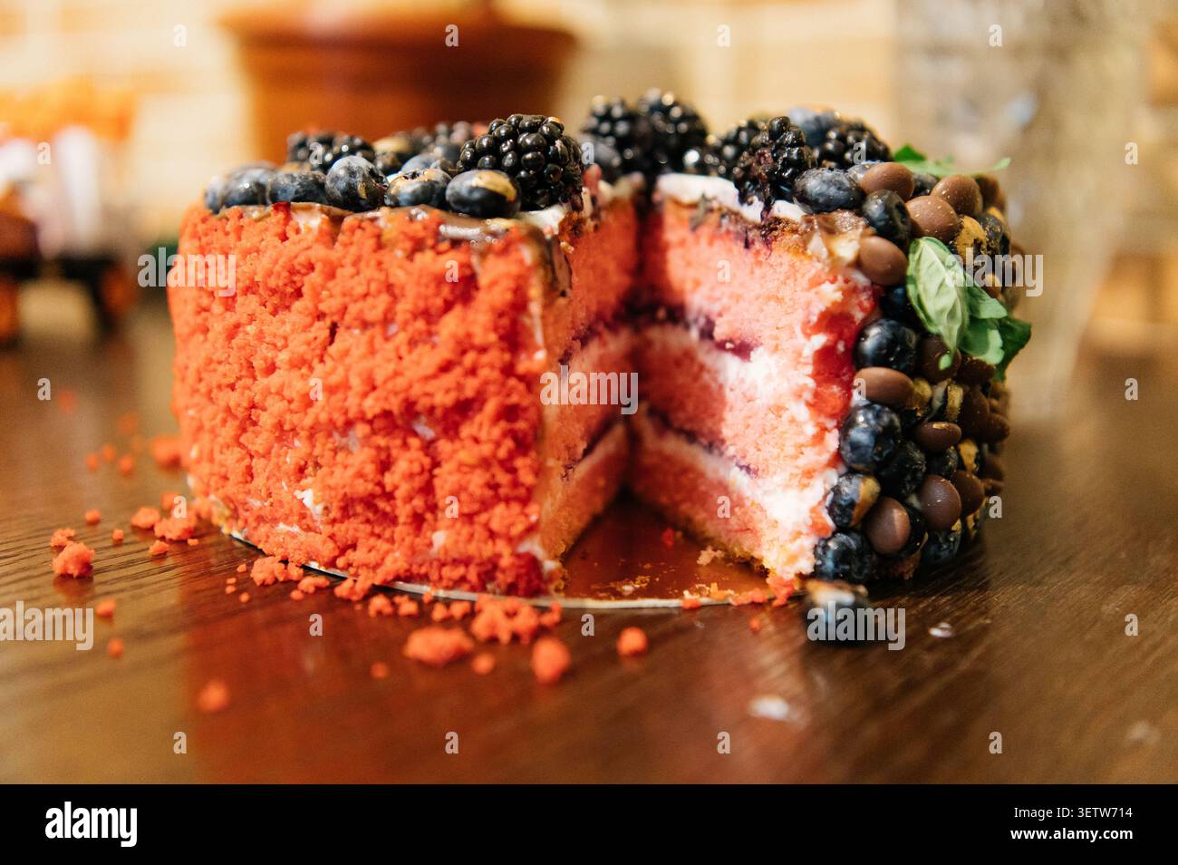 Eine Nahaufnahme eines appetitlichen rosafarbenen Kuchens mit einer geschnittenen Scheibe, bedeckt mit einer strukturierten roten Krümelbeschichtung und einem großzügigen Sortiment Stockfoto