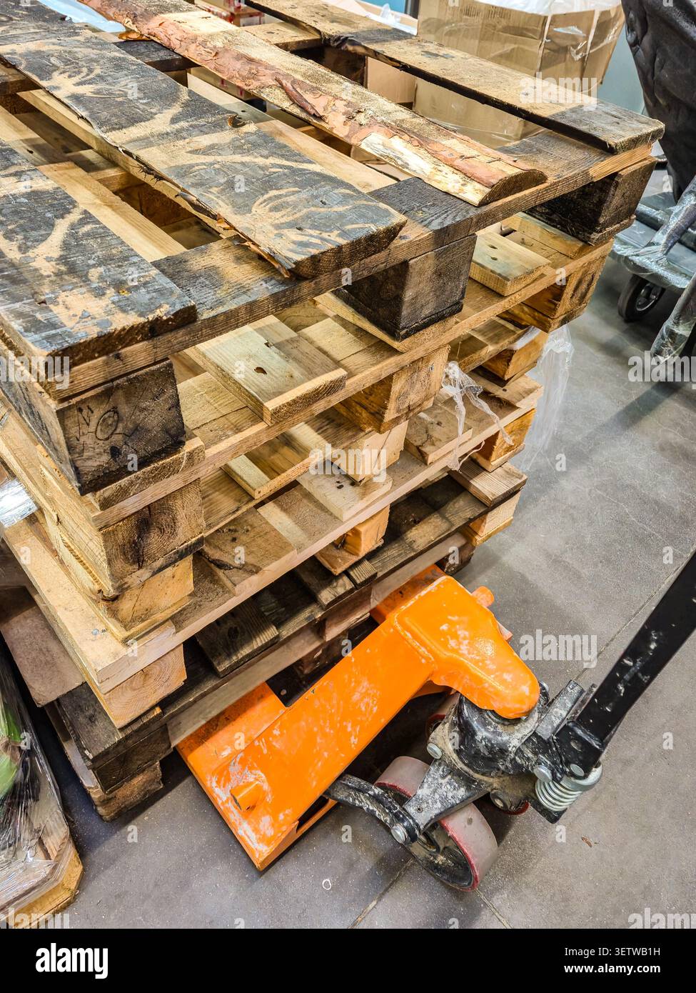 Eine Nahansicht zeigt einen Stapel verwitterter Holzpaletten mit einem orangefarbenen manuellen Palettenheber darunter, der für den Transport von Waren bereit ist Stockfoto