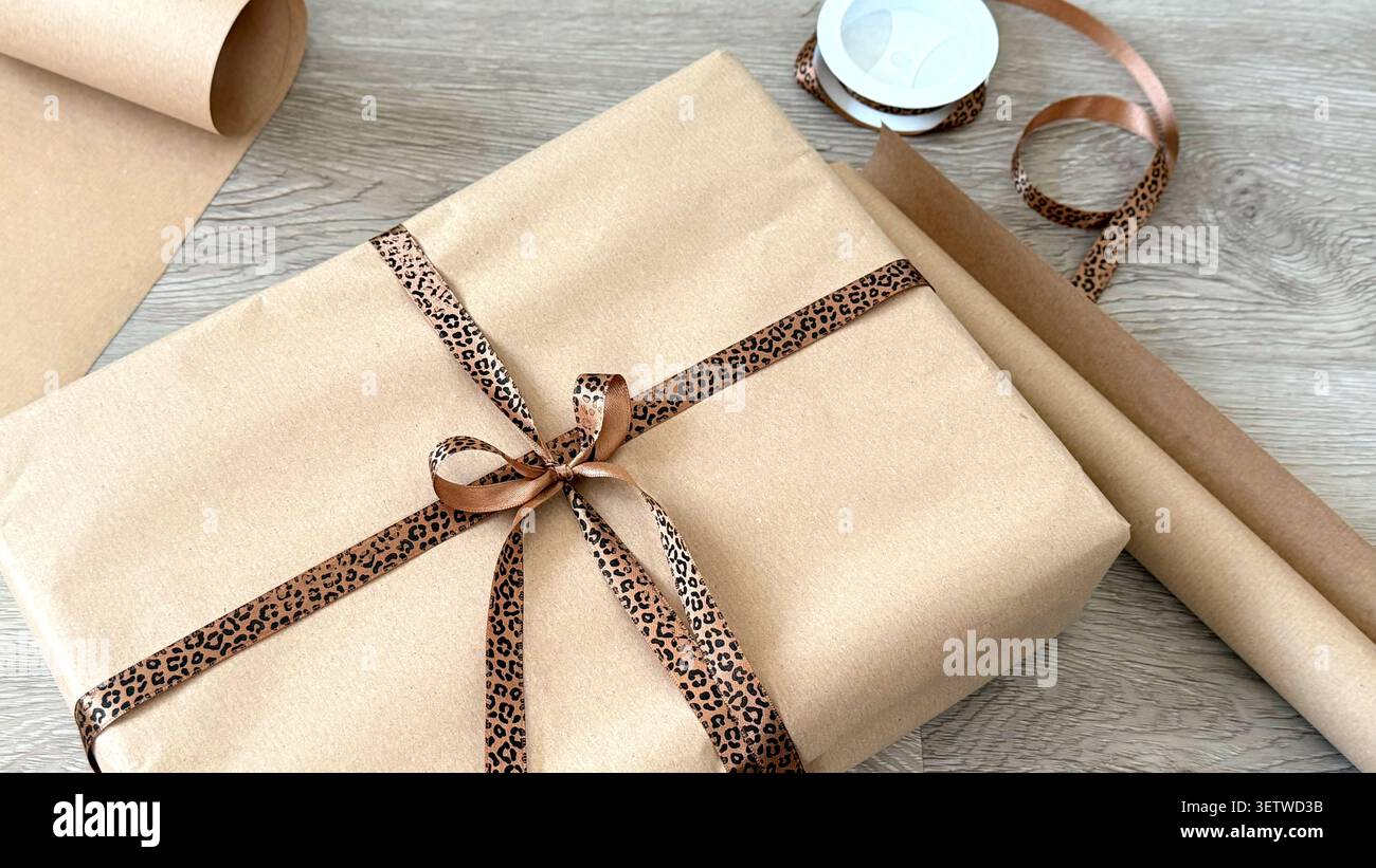 Geschenkbox in braunem Kraftpapier mit Leopardenband und einer Rolle passendes Geschenkpapier auf einer Holzoberfläche Stockfoto