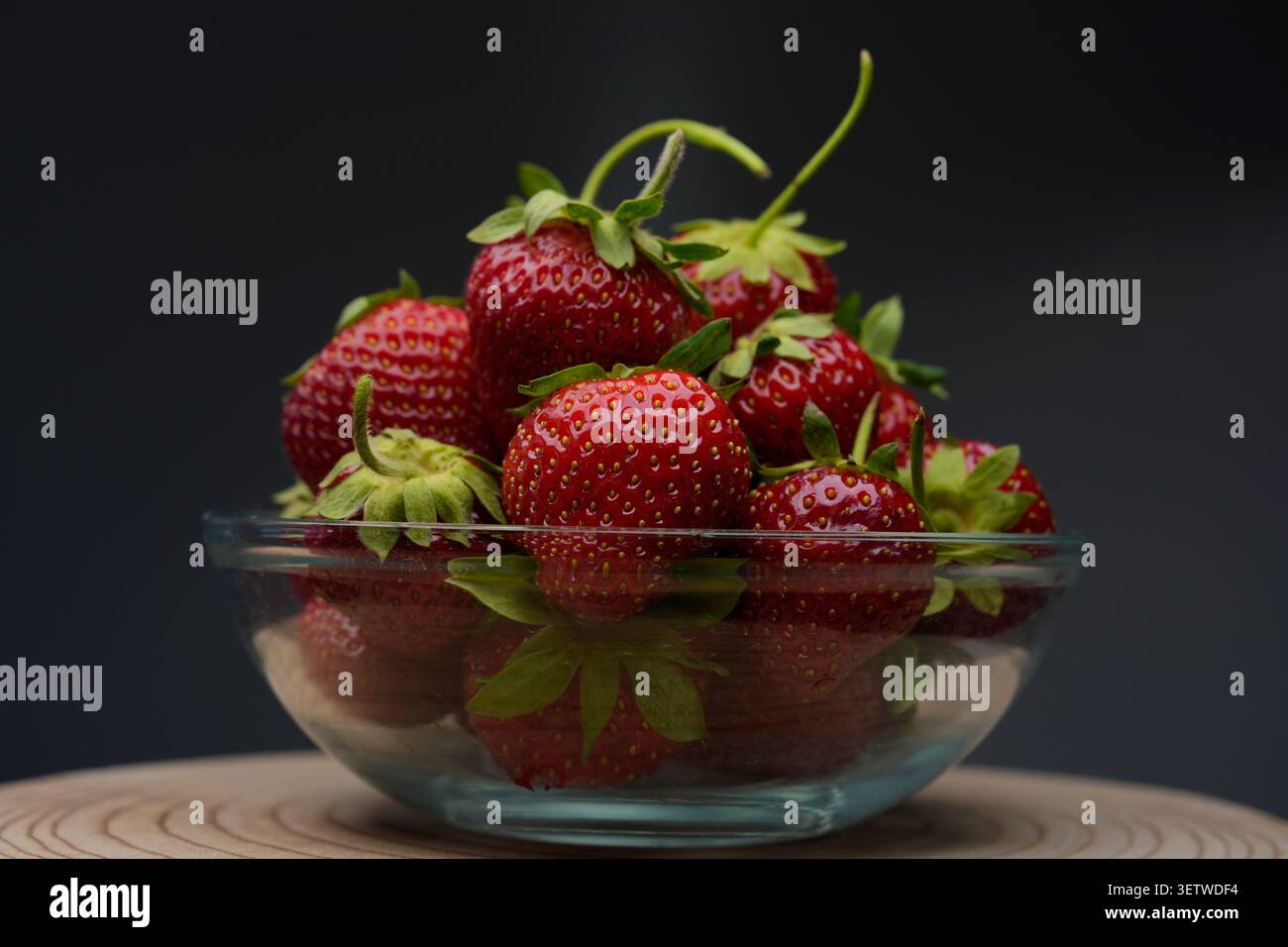 Rote Erdbeeren in Glasschale auf dunklem Hintergrund Stockfoto